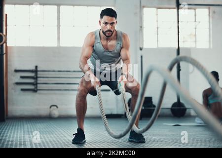 Non arrendete mai. Girato di un giovane uomo utilizzando le corde in palestra per costruire la forza del braccio. Foto Stock