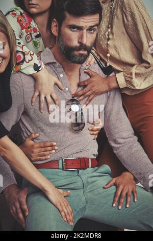 Le Signore mi amano. Studio girato di un uomo attraente in retrò 70s indossare circondato ed essere toccato da donne. Foto Stock