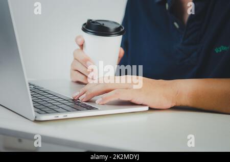 uomo che usa computer portatile e carta da caffè che cerca in internet, invia sms, usa sms messenger o online banking sulla scrivania. Foto Stock