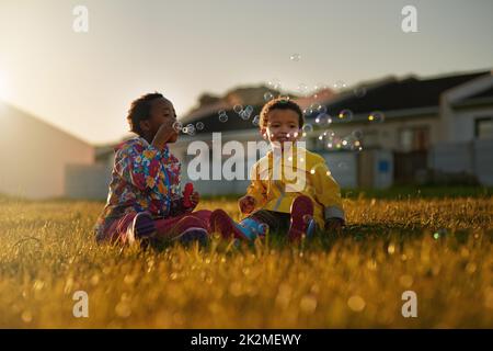 Giocare meglio con le bolle. Colpo di un fratello e di una sorella seduti a terra all'esterno soffiando bolle. Foto Stock