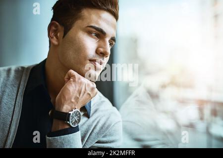 Chissà dove il successo lo porterà alla prossima. Shot di un giovane uomo d'affari che guarda attentamente fuori dalla finestra in un ufficio. Foto Stock