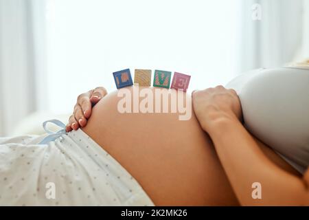 Ho già tanto amore per te. Primo piano di una donna incinta sdraiata con blocchi di legno per bambini sul ventre. Foto Stock