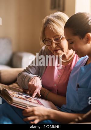 Gli esercizi di memoria sono molto importanti per la loro salute. Scatto di un'infermiera e di una donna anziana che guarda insieme un album fotografico. Foto Stock