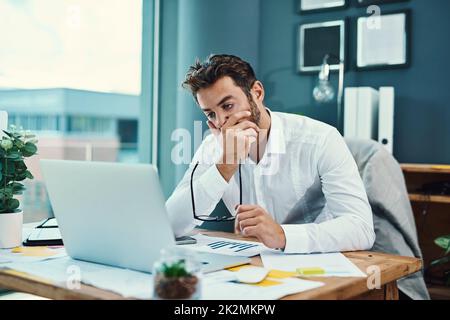 HES trova difficile rimanere concentrati. Scatto di un giovane uomo d'affari che guarda stressato mentre lavora su un notebook in ufficio. Foto Stock