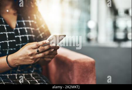 Buone donne d'affari sono sempre raggiungibili. Immagine ritagliata di una donna d'affari irriconoscibile che utilizza uno smartphone mentre si siede su un divano in un ufficio moderno. Foto Stock