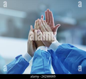 Cooperazione per un'operazione riuscita. Scatto corto di una squadra di chirurghi che si danno a vicenda un alto cinque. Foto Stock