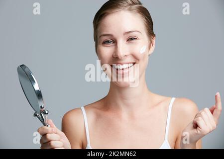 Sia gentile alla vostra pelle. Youve lo ha ottenuto per la vita. Studio ritratto di una giovane donna attraente che tiene uno specchio per le mani e l'applicazione di cosmetici su uno sfondo grigio. Foto Stock