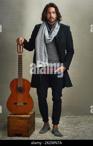 Vestire come youre già famoso. Ritratto di un uomo elegantemente vestito in posa con una chitarra in studio. Foto Stock