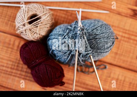 Tutti vogliono un maglione di Natale quest'anno. Foto vita di polpette di lana multicolore e penne per maglieria su un tavolo di legno. Foto Stock