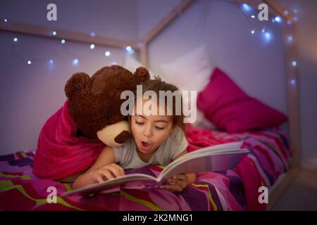 E' una storia piena di meravigliose sorprese. Scatto corto di una bambina che legge un libro a letto con il suo orsacchiotto. Foto Stock