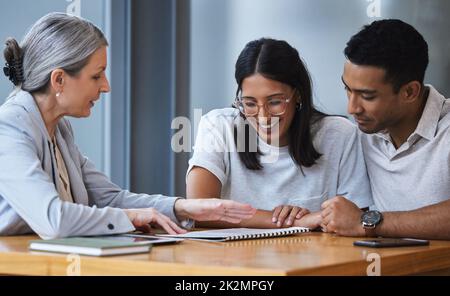 Il nostro emozionante viaggio inizia alla punta di una penna. Scatto di una riunione giovane della coppia con un consulente per discutere il lavoro di ufficio della documentazione. Foto Stock