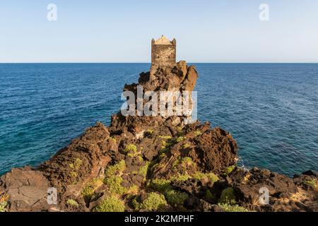 Una torre di guardia medievale arroccata su un affioramento di lava vulcanica che domina il Mar Ionio, vicino al piccolo villaggio di Santa Tecla, Acireale, Sicilia Foto Stock