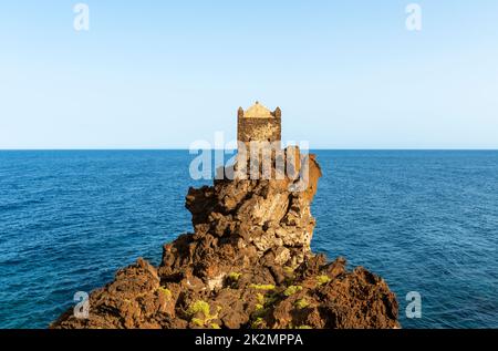 Una torre di guardia medievale arroccata su un affioramento di lava vulcanica che domina il Mar Ionio, vicino al piccolo villaggio di Santa Tecla, Acireale, Sicilia Foto Stock