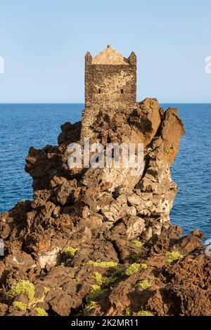 Una torre di guardia medievale arroccata su un affioramento di lava vulcanica che domina il Mar Ionio, vicino al piccolo villaggio di Santa Tecla, Acireale, Sicilia Foto Stock