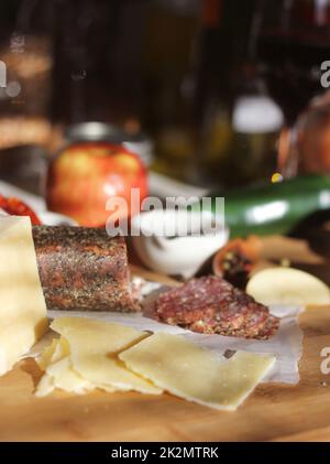 Salame di peppercorn su vassoio con formaggio inglese e irlandese, mele a fette e spezie in cucina rustica Foto Stock