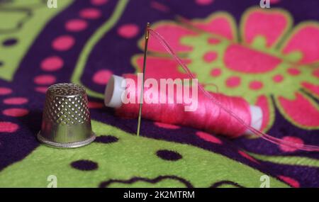 Ditale e rocchetto di filo rosa su tessuto floreale vintage Foto Stock