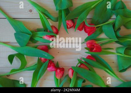 Tulipani rosa con foglie verdi si trovano in un cerchio con un posto libero al centro su uno sfondo di legno Foto Stock