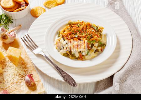 casseruola di fagiolo verde con cipolla francese fritta, parmigiano e cracker guarnire su piatto bianco su tavolo di legno Foto Stock