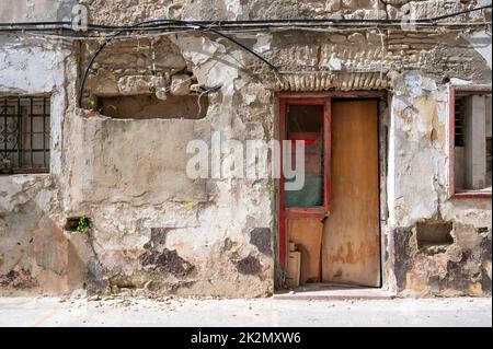 Una vecchia porta di legno con vernice di peeling su un vecchio edificio con una parete bianca e cavi elettrici inchiodati alla parete. Foto Stock