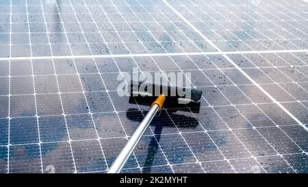 Pulizia pannello solare con mop in microfibra su tetto bagnato. Servizio di manutenzione di pannelli solari o moduli fotovoltaici. Risorsa sostenibile. Energia solare. Verde Foto Stock