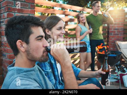 Niente dice fine settimana come un barbecue con gli amici. Shot di un gruppo di amici che hanno birre insieme ad un barbecue. Foto Stock