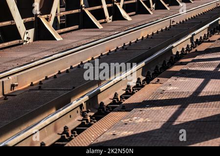 Dettaglio di binari ferroviari sul vecchio ponte metallico, sun gettando ombre su di essi. Foto Stock