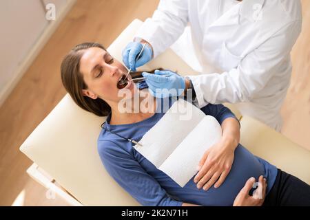 Dentista maschile trattamento denti di giovane donna incinta Foto Stock