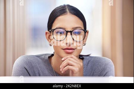 Ive ha preso una decisione da prendere. Scatto corto di una giovane donna d'affari attraente che guarda premuroso mentre lavora sul suo laptop in ufficio. Foto Stock