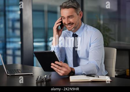 Mi sta guardando la proposta in questo momento. Immagine ritagliata di un bell'uomo d'affari maturo che lavora sul suo tablet mentre effettua una chiamata alla sua scrivania in ufficio. Foto Stock