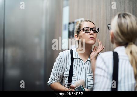 Devo assicurarmi che oggi aspetto il mio meglio. Scatto di una giovane donna d'affari spensierata che guarda la sua riflessione nello specchio al lavoro durante il giorno. Foto Stock