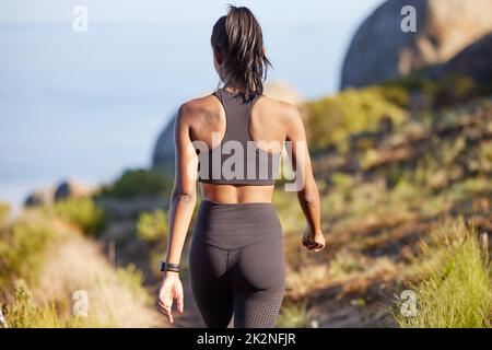 Fuori per una giornata di tonificazione. Ripresa retrospettiva di una giovane donna sportiva che cammina lungo un sentiero all'aperto. Foto Stock