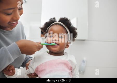 La mamma la aiuterà a mantenere i denti del bambino puliti. Shot di una madre che spazzolava i denti delle sue figlie nel bagno di casa. Foto Stock