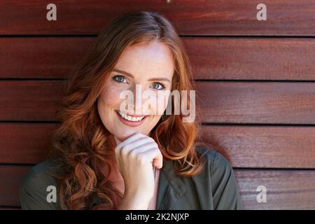 La sua fiducia splende. Ritratto di una giovane donna attraente che si posa contro un muro di legno. Foto Stock