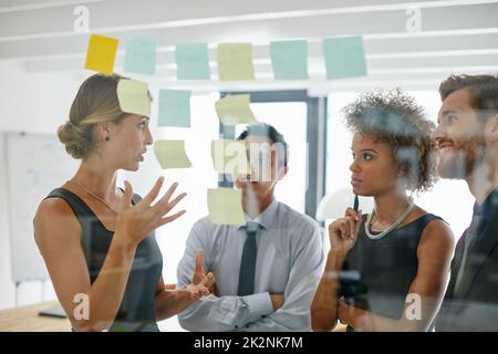 Dietro ogni grande idea c'è una grande storia. Shot di colleghi che utilizzano appunti appiccicosi contro il muro durante una sessione di brainstorming. Foto Stock