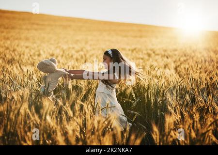 Fuori è il suo posto preferito essere. Scatto di una ragazza piccola carina che gioca con il suo orsacchiotto in un campo di mais. Foto Stock