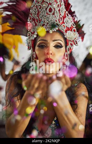 Far rivivere la notte. Colpo di una ballerina samba che soffia i confetti dalle mani mentre si esibisce in un carnevale. Foto Stock