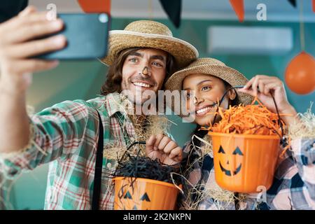 Tutti gli ossequi, nessun trucchi quest'anno. Scatto di una giovane coppia che prende selfie mentre tiene secchi a casa. Foto Stock