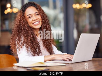 Mantenere la mia attività ovunque. Scatto di una giovane donna d'affari che usa un computer portatile mentre lavora in un bar. Foto Stock