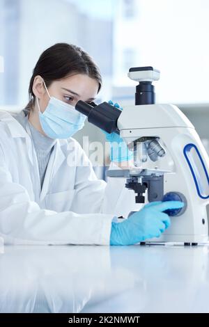 Sembra molto diverso sotto l'obiettivo. Scatto di una giovane donna utilizzando un microscopio in un laboratorio. Foto Stock