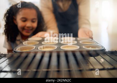 Questi saranno deliziosi. Shot di una bambina che guarda sua madre prendere una teglia da forno. Foto Stock