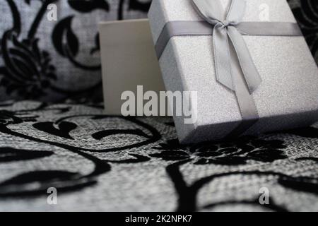 Rivestimento in argento del regalo su sfondo grigio-nero. Foto Stock