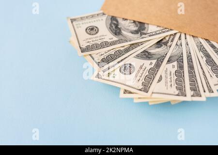 Stash di soldi nelle fatture del dollaro che escono da una busta su uno sfondo blu. Il concetto di stipendio, tangente, prestito, debito, vittoria. Foto Stock