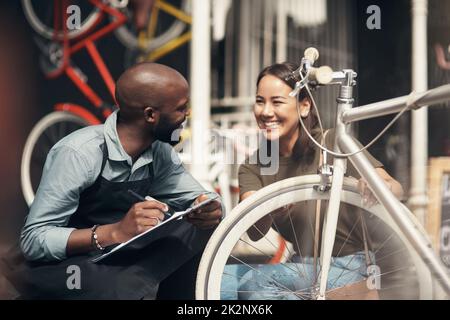 Non vedo l'ora di portarlo a casa. Scatto di un bel giovane uomo che si accoccolava fuori dal suo negozio di biciclette e che assisteva un cliente. Foto Stock