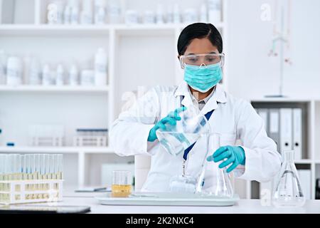 La soluzione è nelle vostre mani. Shot ritagliato di una giovane e attraente scienziata che trasferisce un liquido limpido da un becher a una beuta conica mentre lavora in laboratorio. Foto Stock