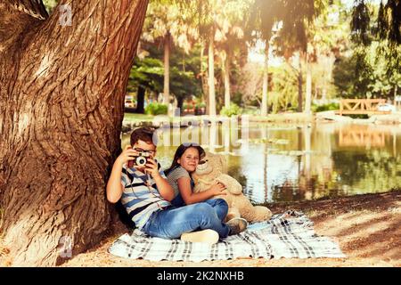 Se potessimo giocare fuori tutto il giorno. Ritratto di due piccoli fratelli che si divertono seduti su una coperta al parco. Foto Stock