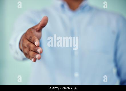 Benvenuto. Scatto corto di un uomo d'affari irriconoscibile in piedi con la sua mano tesa per una stretta di mano su uno sfondo blu. Foto Stock