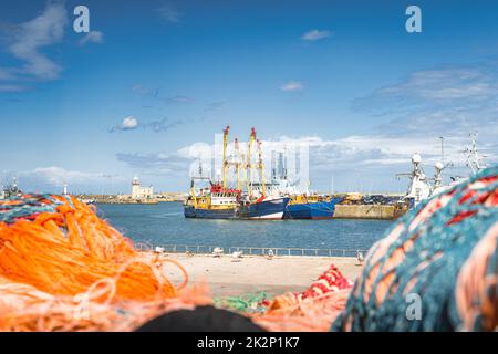 Grandi barche da pesca ormeggiate nel porto di Howth visto attraverso reti sfocate Foto Stock