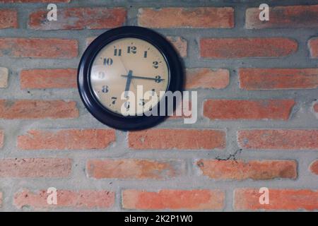 L'orologio nero si trova sul vecchio muro di mattoni. Foto Stock