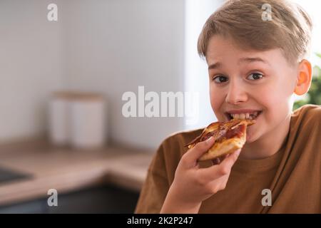 Buon adolescente gustando una deliziosa pizza a casa. Pizza al peperone appena sfornata Foto Stock