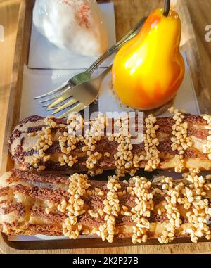 Deliziose torte fresche, eclarie e dessert a forma di pera su un piatto di legno con forchette, dolciumi Foto Stock